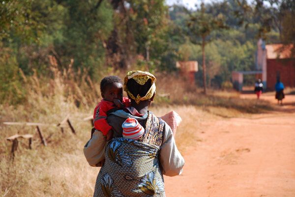 Mulher com criança às costas numa estrada rural em Moçambique