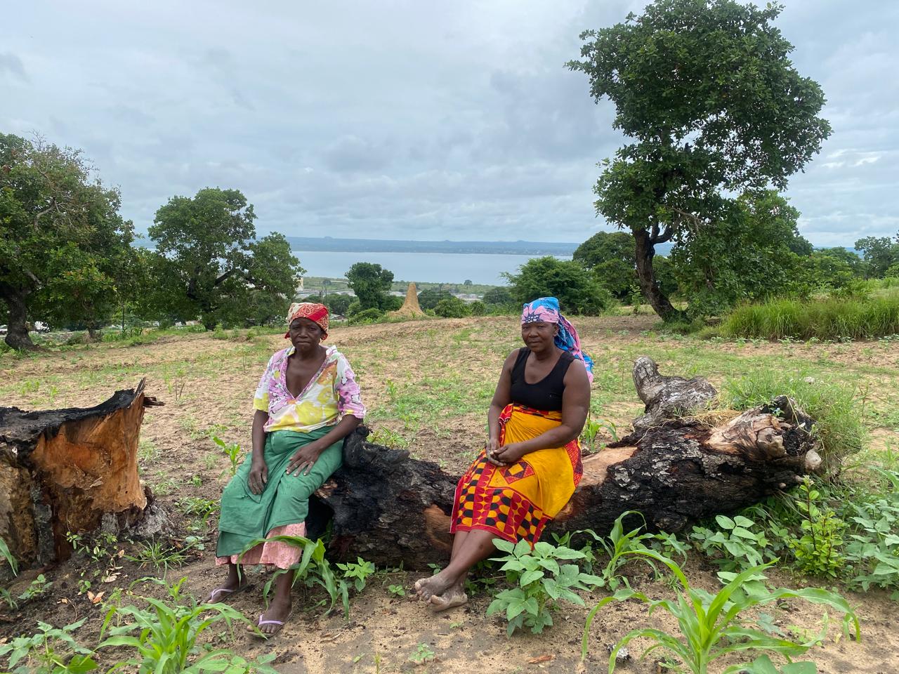 Duas mulheres da comunidade sentadas num tronco, com paisagem ao fundo